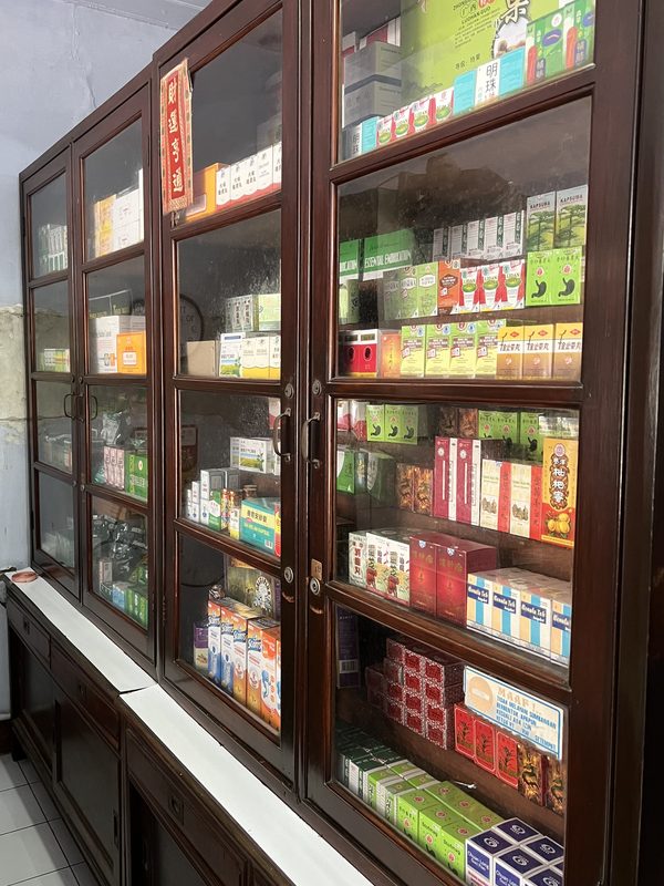 Lemari kaca kayu berisi aneka kemasan obat tradisional Cina dan herbal.